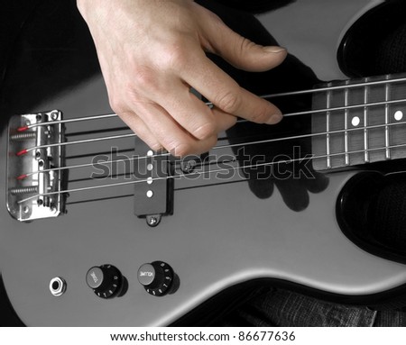female hand on the detail of a black bass guitar in dark back