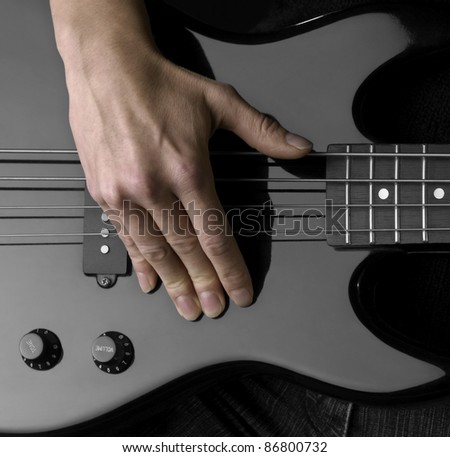 female hand on the detail of a black bass guitar in dark back