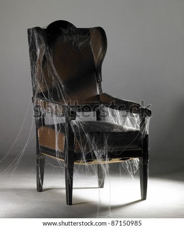 studio photography of a old nostalgic wing chair covered with artificial cobwebs in illuminated grey back
