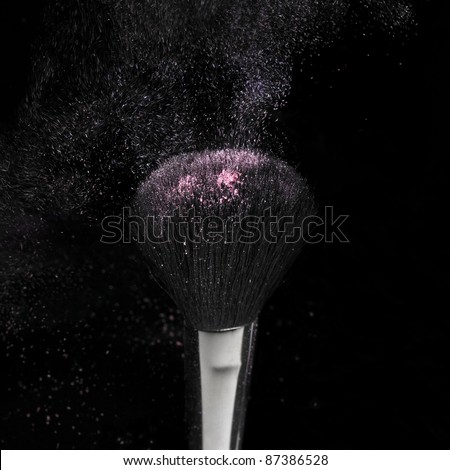 studio shot of a dark brush with floating pink powder particles in black back