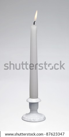 Studio shot of a a white burning candle and a white porcelain candle holder in light back