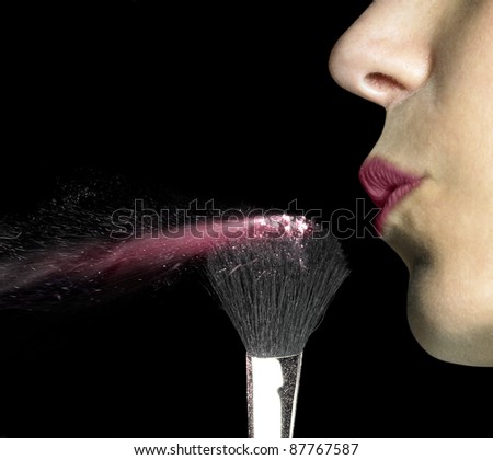 studio shot of a female mouth while blowing on powdered make-up brush in black back