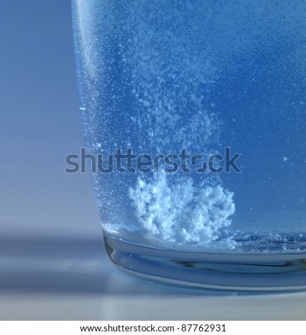 dissolving fizzy tablet floating in a glass of water. Studio photography in blue back