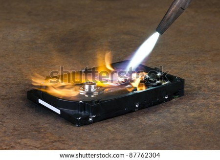 symbolic computer theme showing a welding torch tip and dashing flame burning a fixed hard disk wich is located on rusty metallic ground