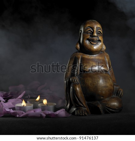 brown Buddha sculpture in dark back with smoke, petals and burning candles