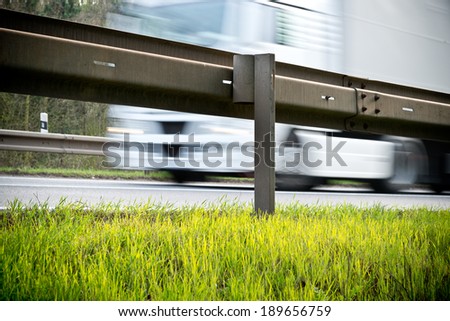 a crash barrier and roadside with going truck