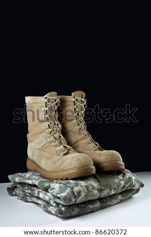 Angled photo of a pairr of tan leather Army combat boots placed together on camouflage uniform on black background