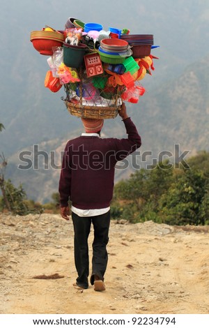 A man is carrying colorful workload on his head and walking on a muddy trail