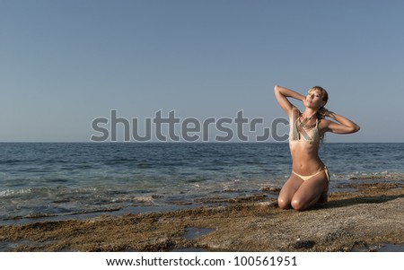Pretty sexy girl in gold bikini like greek goddess posing on a sea reef. Crete. Greece