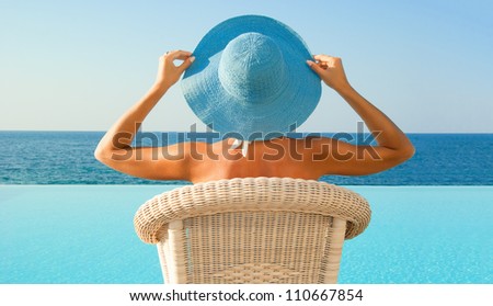 Attractive woman in hat relax near edge of infinity pool and looking to horizon in sunny day. Crete. Greece