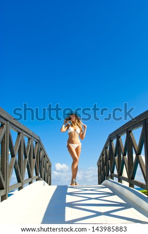 Woman in white bikini look on small bridge and traditional greek bungalow near pool on sunset