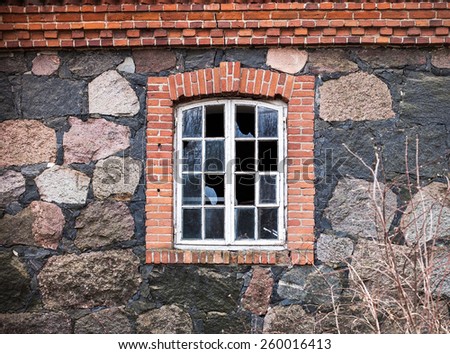 window with broken glass in the wall of the house made of natural stone and red brick