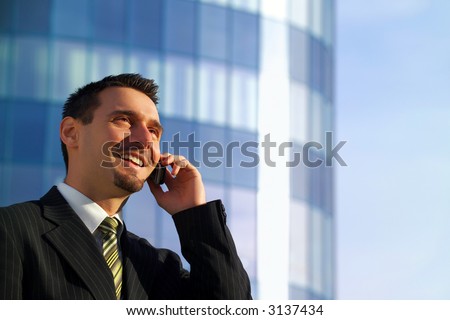Attractive young businessman using a cell phone in front of a modern office building, smiling