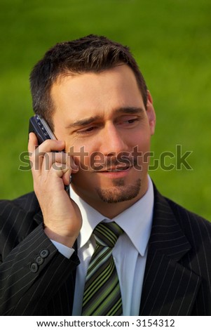 Attractive young businessman using a cell phone, on green background (in a park).