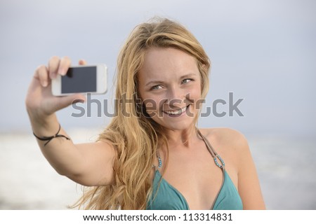 blond woman taking photo with cellphone on the beach