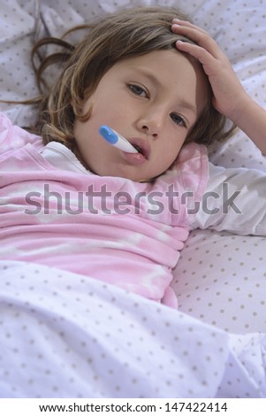 sick girl resting in bed with fever meassuring temperature with thermometer