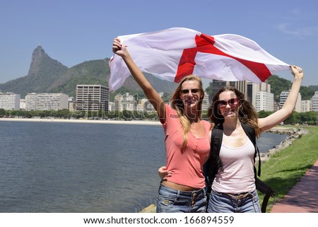 Couple of female sport fans holding the England flag in Rio de Janeiro with Christ the Redeemer in the background.