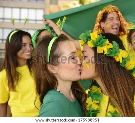Cheerful couple of Brazilian girlfriends soccer fans kissing each other celebrating victory.