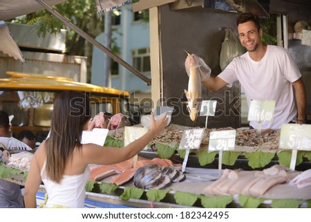 Fishmonger handing out a fish to a customer at an open retail fish market.