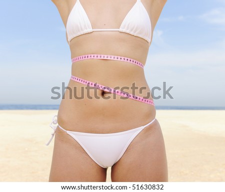 Bikini body:: Young woman with measure tape around her waist on the beach