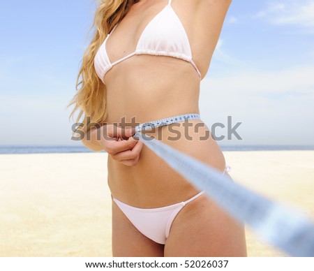 Bikini body:: Young woman wearing bikini measuring her waist on the beach