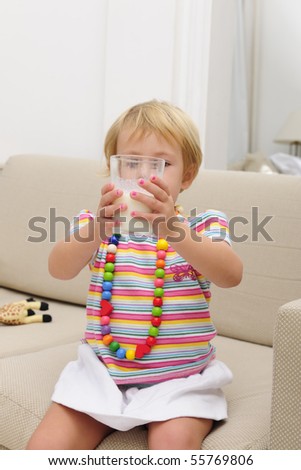happy smiling cute blond child drink a glass of milk sitting sofa in the living room