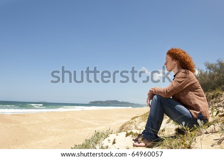 pensive woman sitting on the dunes watching the sea