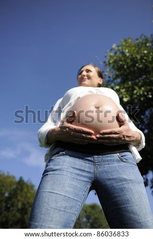 happy pregnant woman holding her belly outdoors
