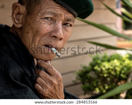 MAE TAN NOI, THAILAND - MARCH 22 2015: Elderly Thai Man, sits and smokes at remote train station Mae Tan Noi on one of the hottest recorded days in Northern Thailand.