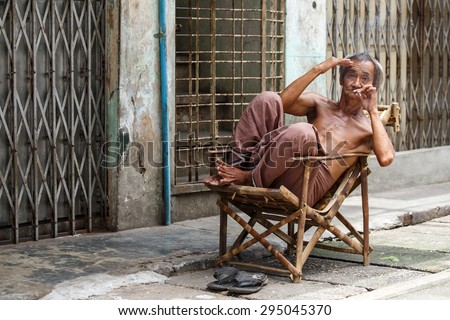 YANGON, MYANMAR - JUNE 12 2015: Old man smoking burmese cheroot cigar on one of the hottest recorded days before monsoon season in Yangon, Myanmar.