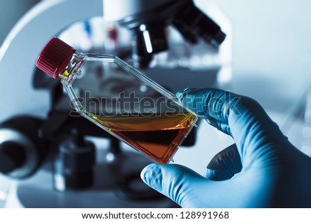 Scientist in laboratory with a culture flask in his hand and a microscope and tubes in background