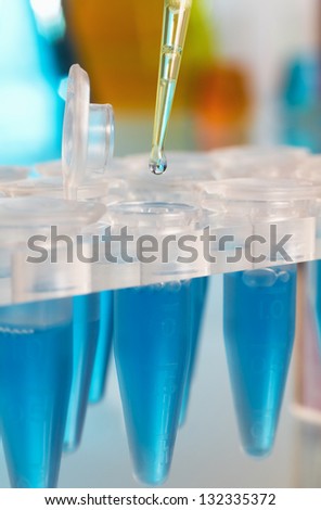 Detail of laboratory pipette with drop of blue reagent depositing over tubes rack