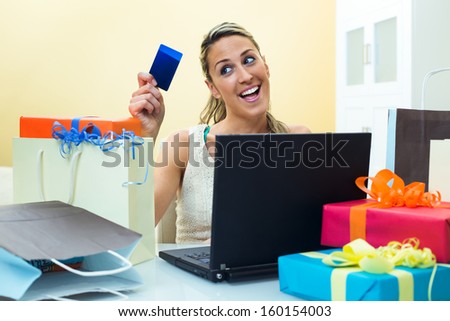 Happy woman shopping online at computer holding credit card and the table full shopping bags
