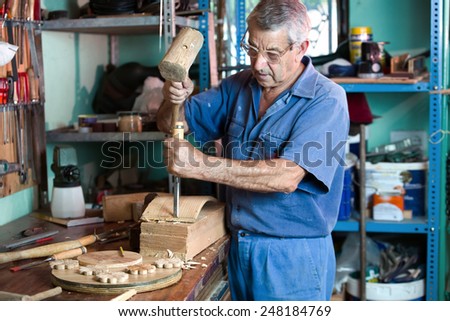 carpenter in the workshop garage handling a chisel and a hammer on a piece of wood / workshop where the cabinetmaker carving wood
