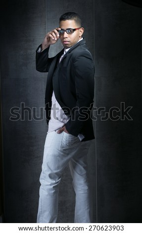 young man latin with casual dress fashionable and glasses looking back in front of a dark gray wall / Trendy man young looking backwards