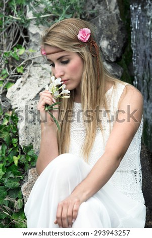 beautiful and sensual woman with long blond hair smelling some flowers from the garden / melancholic portrait of cute blonde woman smelling flowers