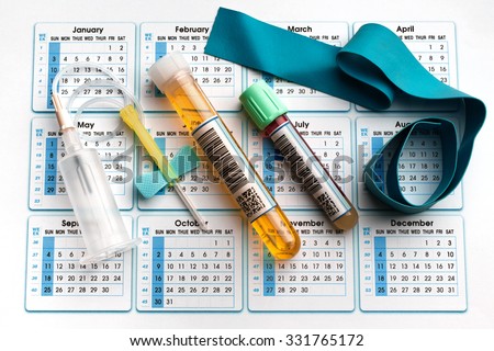 blood tube, urine test, needle and tourniquet on the bottom of an appointment calendar in lab table / equipment for analysis on the daily schedule