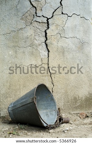 Old broken bucket in front of cracked wall of well