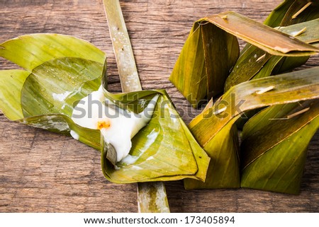 Thai traditional dessert made from coconut pudding, flour, sugar and wrapped in banana leaves with long coconut leaves tail on wooden table