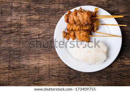 Thai street food style, roasted pork with white sticky rice in white plate on wooden table