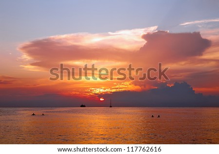 Beautiful sunset in tropical sea. Silhouettes of ships and bathers