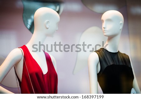 Two woman mannequins in red and black dresses in shopping window in store (selective DOF)