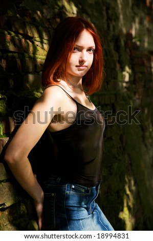 Young red-haired dressed woman on dirty brickwall
