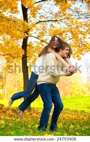 Happy young couple play piggyback in the autumn park