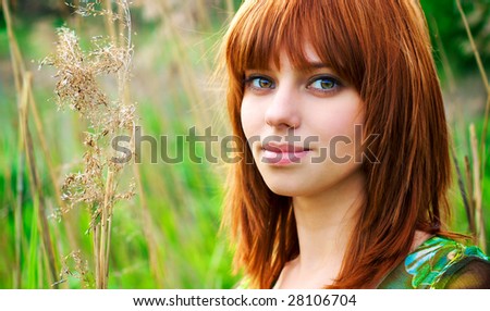 Portrait of a young beautiful woman with red hair in thick grass