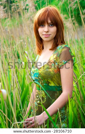 Portrait of a young beautiful woman with red hair  in thick grass
