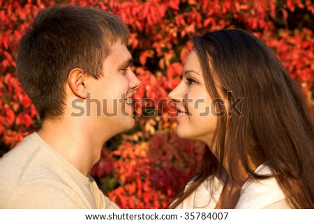 Happy young couple face to face in the autumn park with red leaves