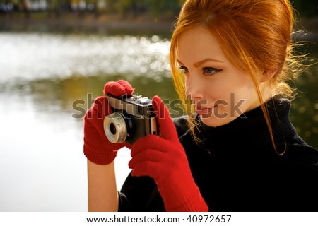 Portrait of a beautiful red-haired girl in red gloves with a camera