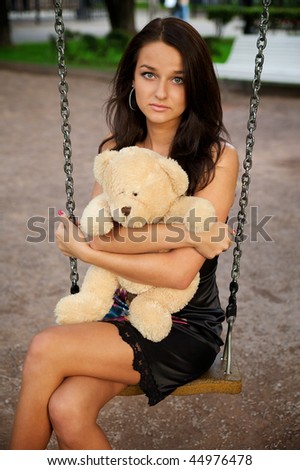 Portrait of a beautiful young woman sitting on a swing with a teddy bear