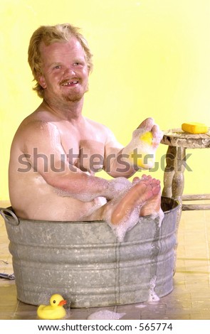 Tiny man takes a bath in a bucket of soapy water with a rubber ducky